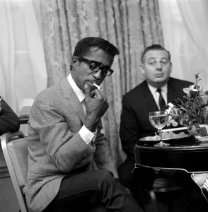 00077 Prints: Sammy Davis Jnr. lights a cigarette in a London restaurant whilst having lunch with