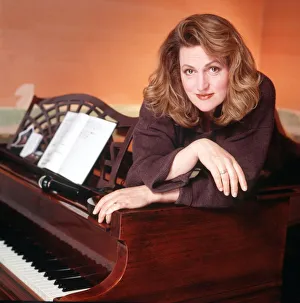 Scottish singer and actress Barbara Dickson poses draped over a piano