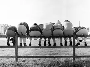 Seven young apprentice female jockeys sitting on a wooden fence during their training