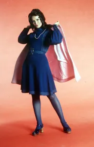 Seventies fashion 1970s model wearing blue A-line dress with sandals and pink cape