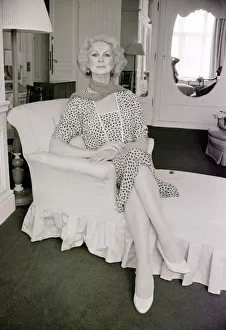 1980s Fashion Prints: Sex change model April Ashley sitting on a recliner wearing a print dress hands clasped