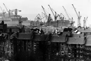 Cranes Prints: Shipyard cranes rise above tenement apartment buildings by the River Clyde in Scotland