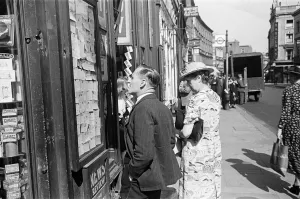 00447 Prints: Shoppers looking for a bargain read the small ads outside a Earls Court News Agents