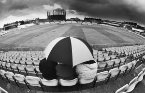 00436 Prints: Spectators sit out showers underneath an umbrella as they wait for Pakistan