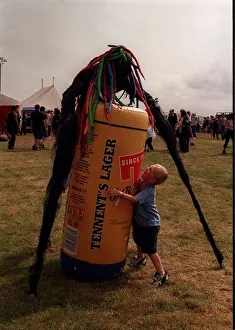 Stilts Prints: Stilted figure at T in the Park wearing a bright coloured wig standing over an inflatable