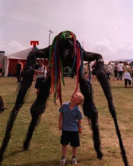 Stilts Prints: Stilted figure towering over a small boy at T in the Park wearing a bright coloured wig
