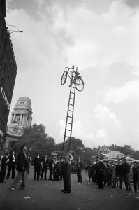 Street Scenes Prints: A street entertainer at Tower Hill, London balancing a bicycle on a ladder using his chin