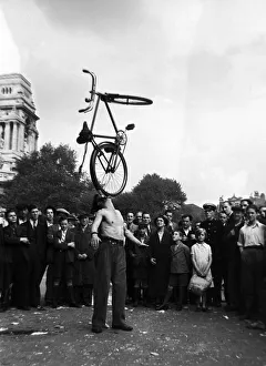 Skill Prints: A street entertainer at Tower Hill, London balancing a bicycle using his mouth watched by