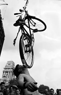 A street entertainer at Tower Hill, London balancing a bicycle using his mouth watched by
