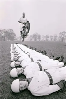Stuntman Prints: Stunt team in action 1966. Man leaps on a motorcycle over men lying on the ground