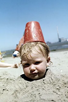 Toddler Prints: Summer holidays July 1976 - Boy buried in sand with red plastic Bucket on his head