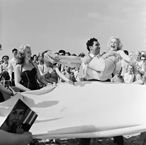 Sunday Pictorial 1957 Beach Party. Angela Manselle being placed on a blanket by Phil