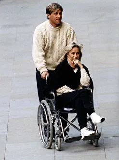 Susan George Actress is pushed along in a wheelchair by her husband Simon MacCorkindale