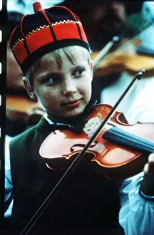 Sweden boy playing violin wearing red and blue traditional hat circa 1990