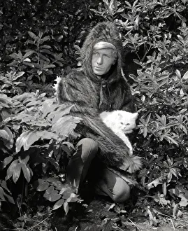 Ted Dawson modelling a fake fur coat with a hood for men while holding a white furry cat