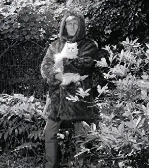 00186 Prints: Ted Dawson modelling a fake fur coat with a hood for men while holding a white furry cat
