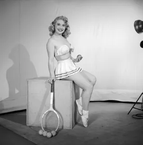 Anyone for tennis? Woman wearing bra, skirt holding tennis racket. 1959