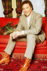 Tom Jones singer sitting on red sette pale suit polo neck jumper glass boots tartan