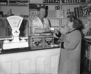 Scales Prints: Tom Slinn, cut price grocer, seen here behind the counter serving a customer at his shop