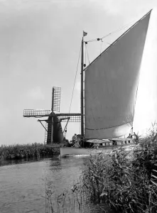 A traditional Norfolk Broad yachts sailing past one of the many windmill water pumps that