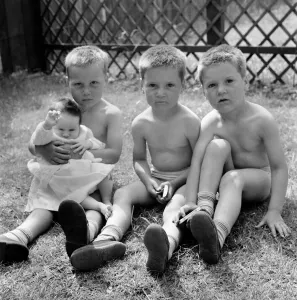 Three triplet brothers holding their new born baby sister in the garden of their home in