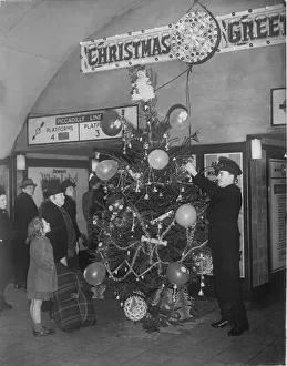 Shelter Prints: An underground railway guard decorating a Christmas tree at Holburn tube station during