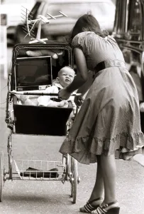 Unusual - Mother pushing a pram with her baby and a portable television set placed next