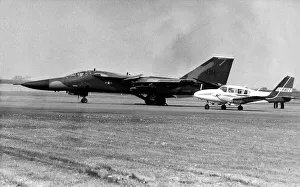 00347 Prints: A USAF General Dynamics F-111 Aardvark sits on an airfield next to twin engined civil