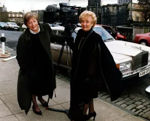 Vera Weisfeld black cape brown suit beside television camera Rolls Royce car