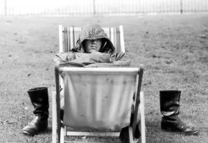 A weary traveller removes his boots as he takes a rest on a bed made from two deckchairs