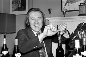 Wine: Mr. David Frost trying to open a bottle of wine at his home. March 1975 75-01338