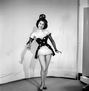 Torch Prints: Woman cinema usher wearing star pattern top hat and dress holding a torch. 1959 E41