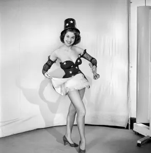 Woman cinema usher wearing star pattern top hat and dress holding a torch. 1959 E41