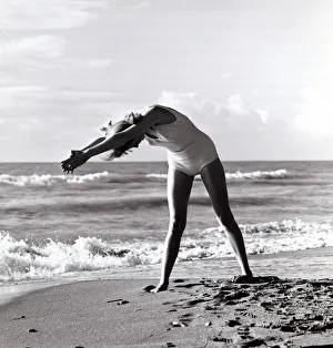 Stretching Prints: Woman exercising on beach. December 1964 1960s *** Local