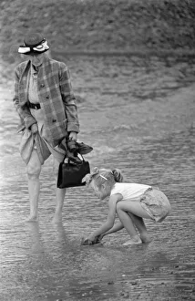 Waves Prints: A woman goes for a paddle in the sea as a young gurl picks up a handful of sand