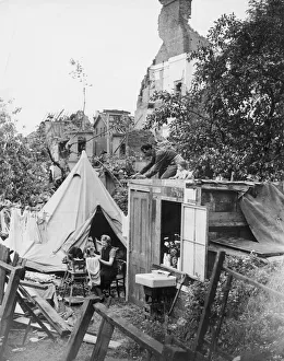 Housework Prints: A woman sewing her clothes using a sewing machine as she sits amongst the destruction of