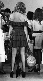 Queues Prints: Woman standing in a queue wearing a strapless black dress as a cat gets in on the act
