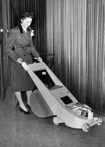Household Prints: A woman trying out a stream lined lawn mower which can be driven by petrol or electric