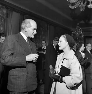 Coat Prints: Woman wearing long coat and hat talking to a man wearing a suit at a cocktail Party