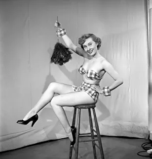 Woman wearing plaid bra and short skirt holding duster. 1959