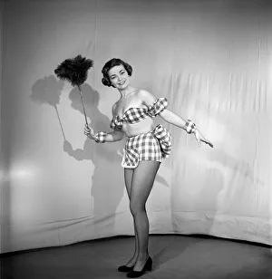 Woman wearing plaid bra and short skirt holding duster. 1959
