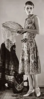 1926 Prints: A woman wearing white and gold brocade evening gown which has a tight bodice