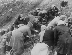 Women with buckets, bags and sacks scrounge for pieces of coal amongst the slag