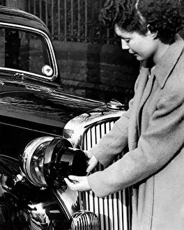World War II: Blackout. Woman fitting blackout shields to the headlamps of her car