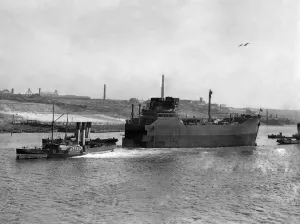 00037 Prints: World War II Shipbuilding. Tugs pull The bow Section of a new cargo ship along the river