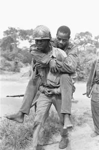 Wounded Prints: A wounded Biafran soldier is given a piggy-back to a field dressing station following an