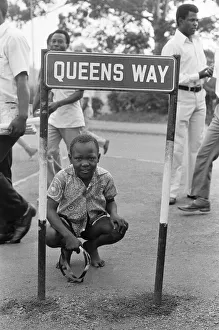 One Boy Only Prints: Young boy kneeling down bya road sign reading Queens Way'in Kampala, Uganda
