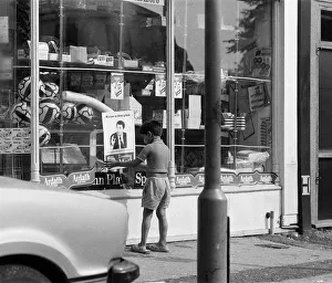 Poster Prints: A young boy puts up a Muhammad Ali poster on a shop window in Birmingham