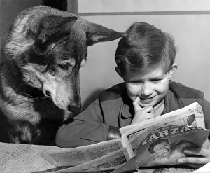 A young boy reading the newspaper watched by his pet dog December 1952