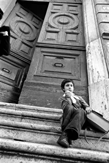 00067 Prints: Young child sitting on the steps of an old building in a poor suburb on the outskirts of